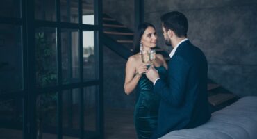 Successful couple in classy attire standing inside a multi million dollar house drinking wine.